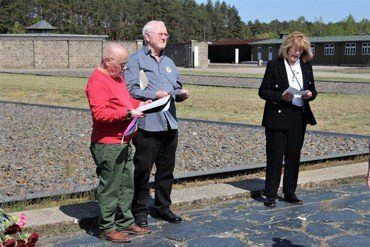 Drei Erwachsene lesen draußen an Bahngleisen.
